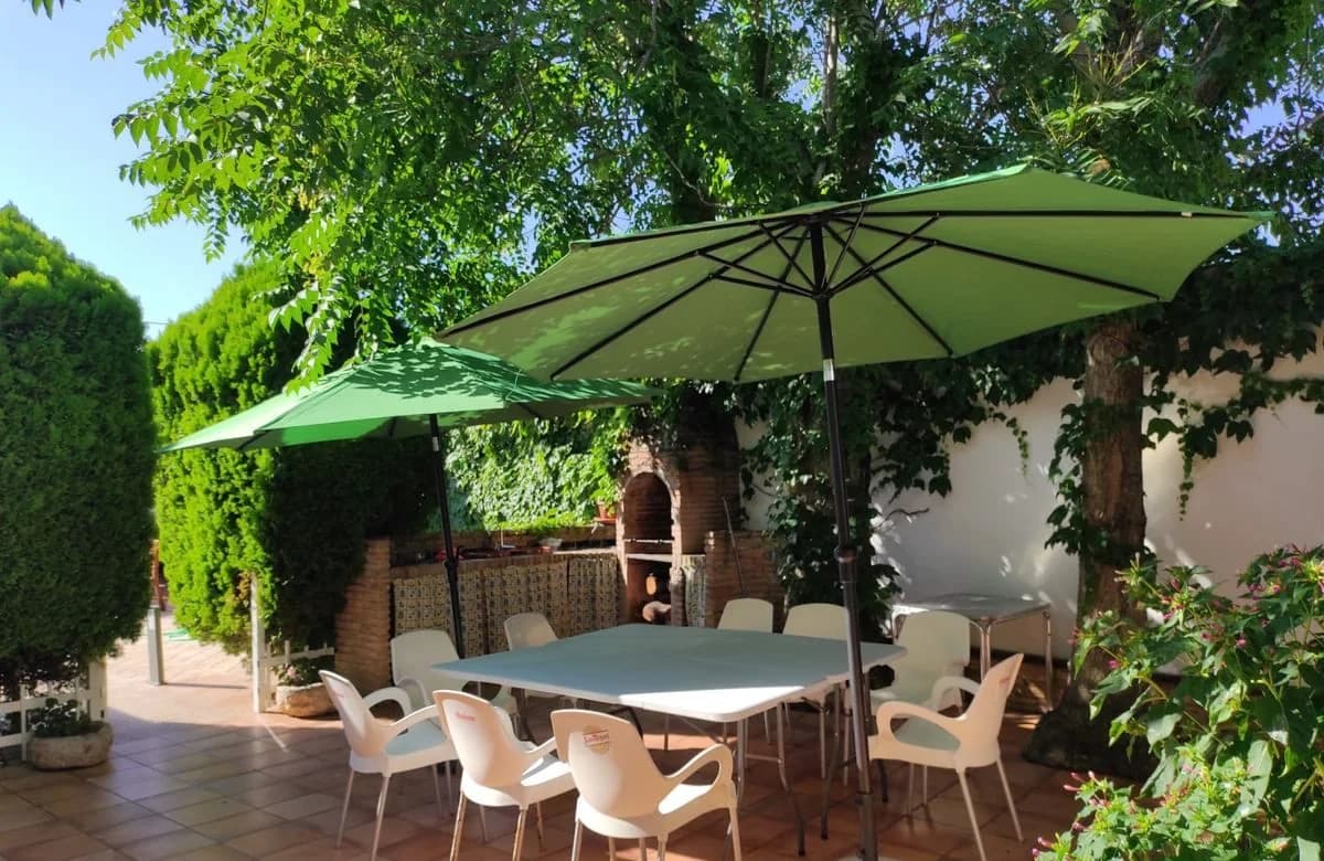 Jardín con árboles, sombrillas verdes y mesa para comer al aire libre