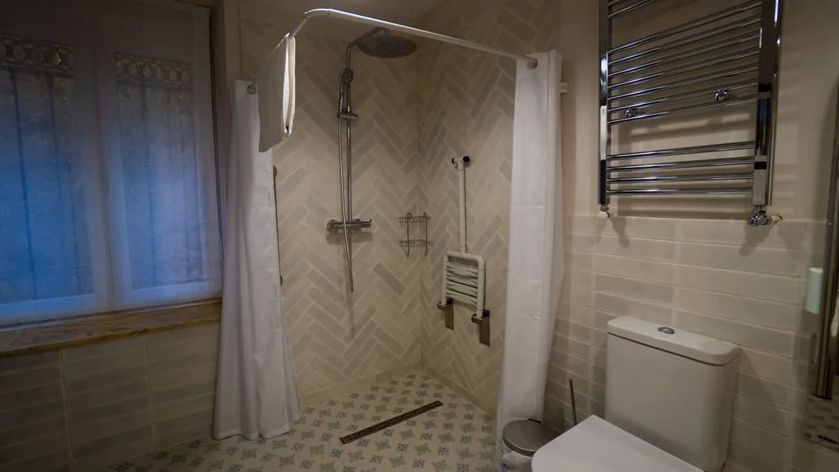 Baño adaptado con ducha a ras de suelo, barras y silla de ducha